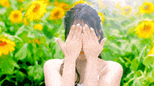 a woman is covering her face with her hands in front of a field of sunflowers