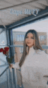 a woman in a white shirt is holding a bouquet of red roses .