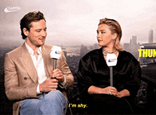 a man and a woman are sitting next to each other and the man is holding a microphone that says capital