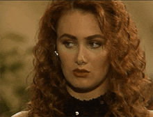 a woman with red hair is wearing a black top and earrings .