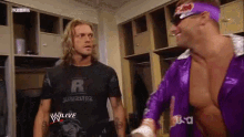 two wrestlers are standing in a locker room and one of them is wearing a purple outfit