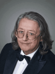 a man wearing glasses and a tuxedo is smiling for the camera