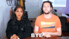 a man and a woman sitting at a table with bye written on the table