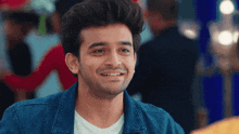a young man wearing a blue denim jacket and a white shirt is smiling