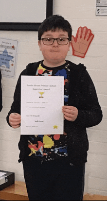 a young boy holds up a certificate that says ' apache green primary school ' on it