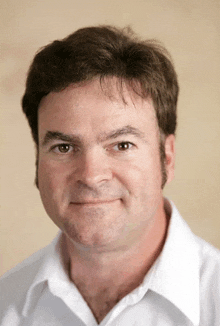 a man in a white shirt looks at the camera and smiles