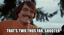 a man with a mustache is smiling with the words that 's two thus far shooter below him