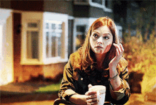 a woman sitting in front of a house with a cup in her hand