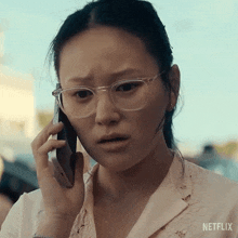 a woman wearing glasses is talking on a cell phone with netflix written on the bottom right