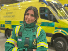 a female paramedic is standing in front of an ambulance with her arms crossed .