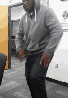 a man wearing a grey hoodie is dancing in a room
