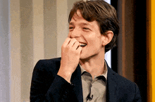 a man in a suit is laughing and covering his mouth with his hands