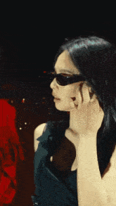 a woman wearing sunglasses and a black dress adjusts her earring