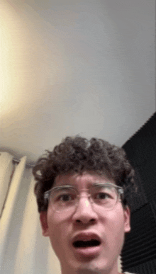 a man with curly hair wearing glasses is making a funny face .