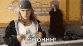 a man with long hair is standing in front of a brick wall with a boombox .