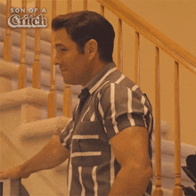 a man in a striped shirt is standing on a set of stairs with the words son of a grifch behind him