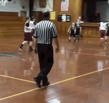 a referee walks across a basketball court with a player wearing a jersey with the number 23