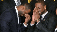 two men in suits and ties are laughing and one is covering his face with his hands