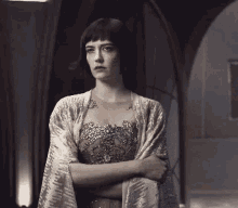 a woman in a dress and shawl is standing with her arms crossed in a dark room .