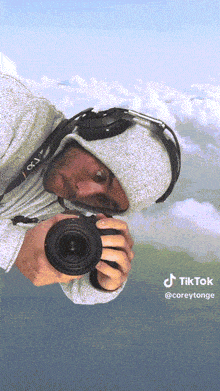 a man in a hoodie is taking a picture with a camera that says canon on it
