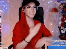a woman wearing glasses and a hat is sitting in a chair on a twitch stream .