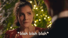a woman is talking to a man in front of a christmas tree and the words blah blah blah are above her .