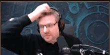 a man wearing headphones and glasses is scratching his head while sitting in front of a microphone .