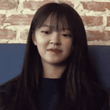 a young woman with long hair and bangs is sitting in front of a brick wall and making a funny face .