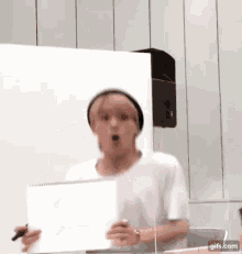 a man in a white shirt and black hat is holding a piece of paper and a pen .