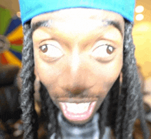 a man with dreadlocks is wearing a blue hat and making a face