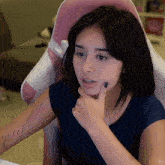 a woman in a blue shirt is sitting in a pink and white chair with her hand on her chin