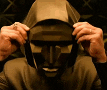 a man is wearing a hooded mask and holding it over his head .