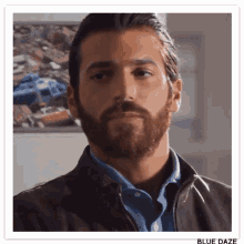 a man with a beard is wearing a brown jacket and a blue shirt