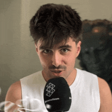 a man wearing a white tank top is holding a black microphone that says genesiscom on it