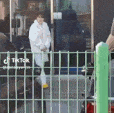 a woman in a white coat is walking behind a fence next to a car .