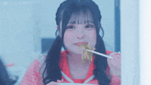 a girl with pigtails is eating noodles with chopsticks and smiling .