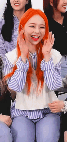 a girl with orange hair is sitting in front of a group of people and smiling