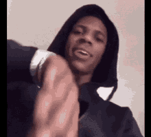 a man in a hoodie is pointing at the camera and making a funny face .