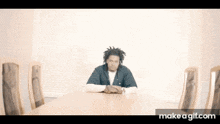a man with dreadlocks is sitting at a table with his hands folded