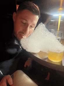 a man sitting at a table smelling a foamy liquid