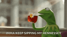 kermit the frog is drinking a cup of tea and says imma keep sipping my hennessey .