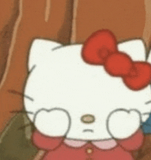 hello kitty is wearing glasses and a red bow and is sitting next to a tree .