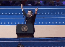 a man standing at a podium with his arms in the air