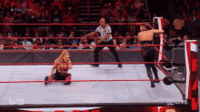 a woman is kneeling down in a wrestling ring while a referee stands behind her .