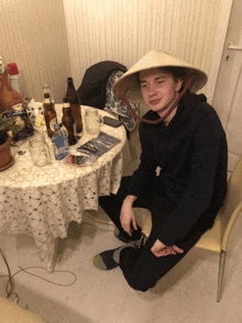 a young man wearing a conical hat sits in front of a table