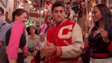 a man in a red and white varsity jacket with the letter c on it is dancing in front of a crowd .