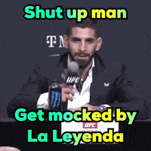 a man in a suit is talking into a microphone with the words shut up man get mocked by la leyenda below him