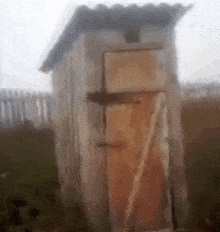 a wooden outhouse in a field with a fence in the background .