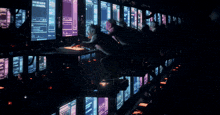 a group of people sitting in front of a row of computer monitors one of which says " the genesis "
