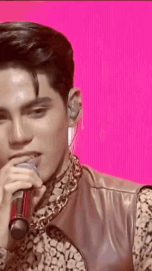a close up of a man singing into a microphone with a pink background